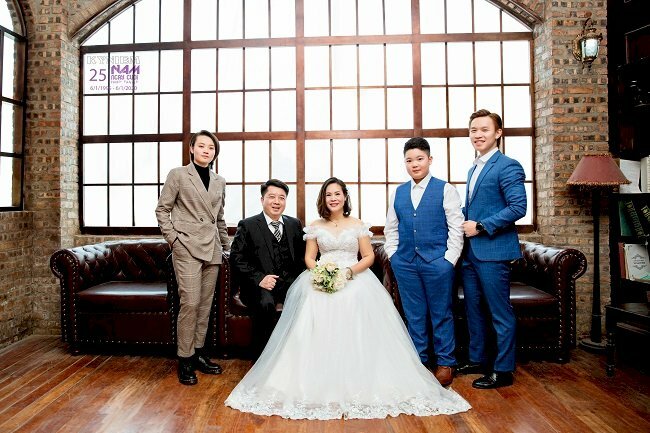 Cách tạo dáng chụp ảnh gia đình 5 người kiểu truyền thống khi mẹ mặc áo cưới, bố cùng các con cùng mặc vest, với kiểu này thì bố và mẹ cùng ngồi trên sofa, 3 con đứng hai bên bố mẹ.