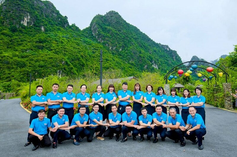 Cách tạo dáng chụp ảnh tập thể công ty đoàn kết bằng cách xếp thành 2 hàng ngang hơi vòng cung, hàng thứ nhất mọi người cùng ngồi xổm, đan tay vào nhau, hàng thứ 2 mọi người đúng và đan chéo tay cầm tay nhau. 