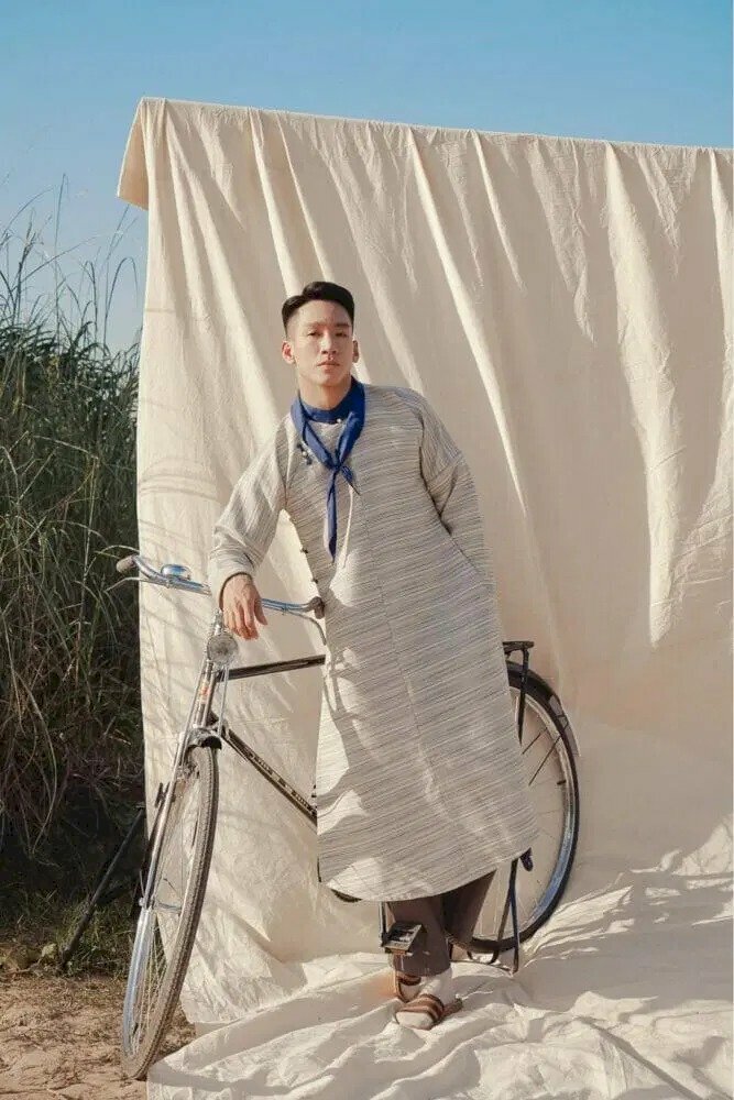 Cách tạo dáng chụp ảnh Tết cho nam với áo dài bên cạnh chiếc xe đạp, đứng tựa người vào chiếc xe, 1 tay đặt lên đầu xe, 1 tay cho vào túi quần.