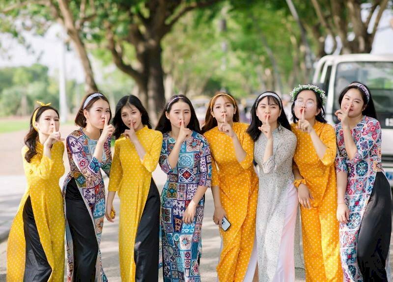 Cách tạo dáng chụp ảnh áo dài tập thể kiểu lầy lội dành cho nhóm bạn nữ 8 người, với kiểu này mọi người cùng xếp thành hàng ngang, đứng hơi chùng gối xuống, đưa 1 ngón tay đặt lên miệng với biểu cảm 'suỵt' nói nhỏ thôi.
