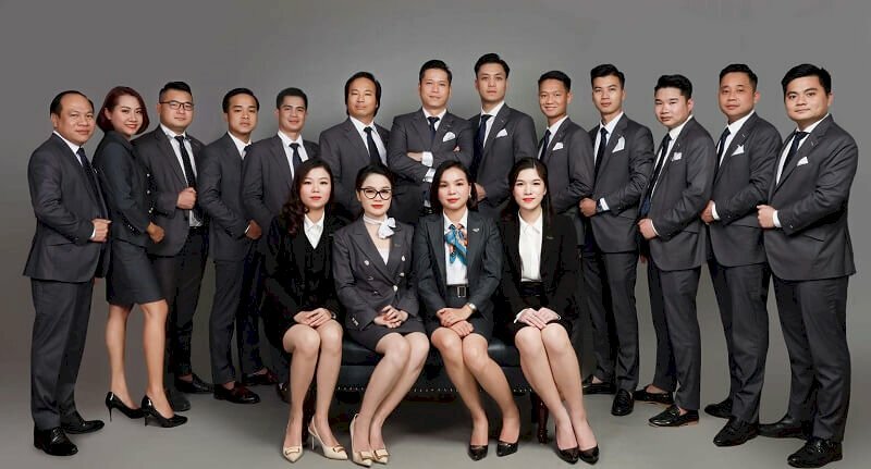 Cách tạo dáng chụp ảnh tập thể công ty với kiểu các nữ sẽ ngồi trên ghế sofa và nam sẽ đứng đằng sau tạo hình vòng cung, tay cầm vạt áo vest.