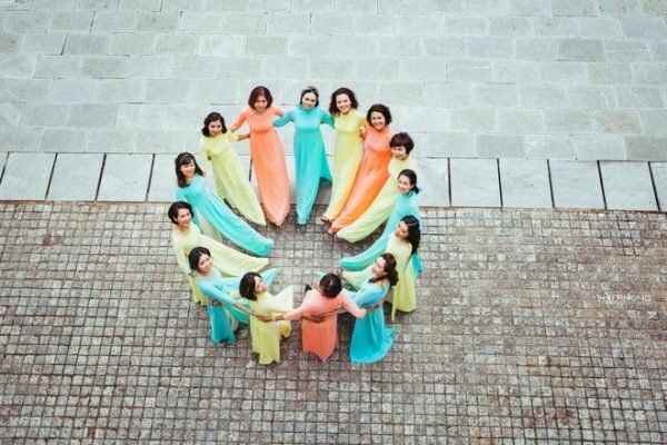 Cách tạo dáng chụp ảnh áo dài tập thể kiểu lầy lội dành cho nhóm nữ trên 10 người, với góc chụp từ trên cao nhìn xuống, mọi người cùng xếp thành hình tròn, tay đan vào nhau, đưa 1 chân vào trong vòng tròn, cùng ngước mặt nhìn lên phía ống kính.
