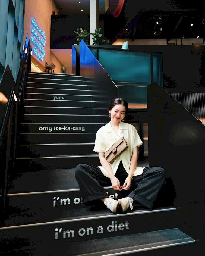 Cách tạo dáng chụp ảnh với cầu cho nữ dễ thương, ngầu chất với dáng ngồi bệt trên bậc thang, hai chân tạo dáng hình cánh bướm và chụm bàn chân vào nhau, hai tay thả lỏng xuống chạm nhẹ vào nhau, đầu hơi nghiêng về 1 bên, mắt nhắm miệng cười mỉm.