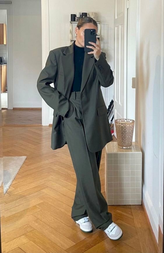 Với bộ vest màu xám đen dài kết hợp cùng đôi giày sneaker hãy tạo dáng chụp hình cá tính với 1 tay bỏ vào túi quần, 1 tay tay cầm điện thoại chụp hình, chân phải bắt chéo qua chân trái.