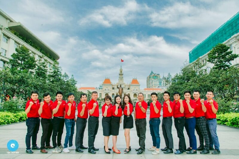 Cách tạo dáng chụp ảnh tập thể công ty xếp thành 1 hàng ngang và mọi người cùng đưa 1 tay nắm chặt hướng lên trời tượng trưng cho sự đoàn kết, sức mạnh, và thách thức.