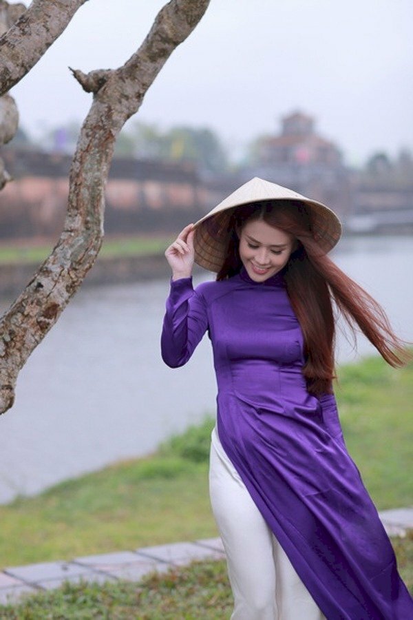 Tạo dáng bước đi nhẹ nhàng, đầu hơi cúi nhìn xuống, một tay vịnh chiếc nón lá, một tay buông tự nhiên