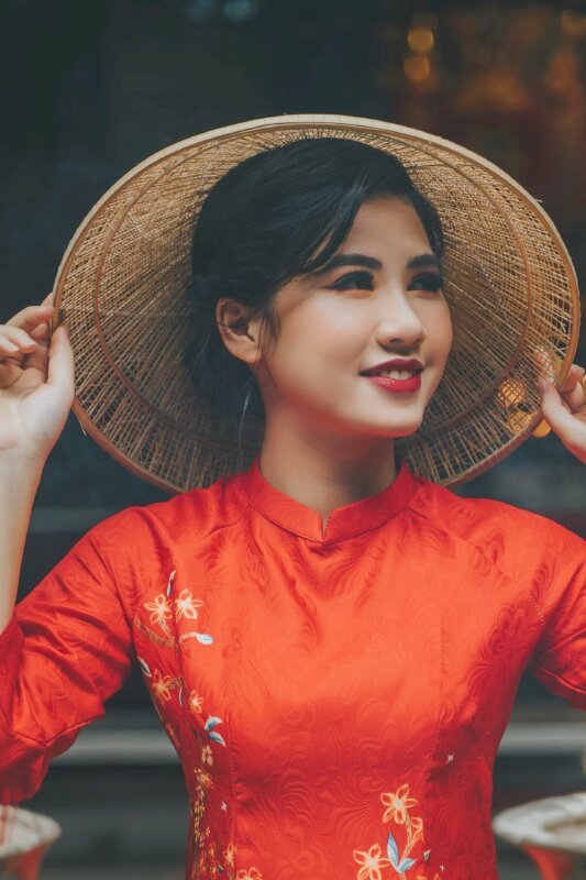 Cách tạo dáng với áo dài cách tân với hai tay vịnh chiếc nón, đầu nghiêng nhìn sang một phía, cười thật duyên dáng