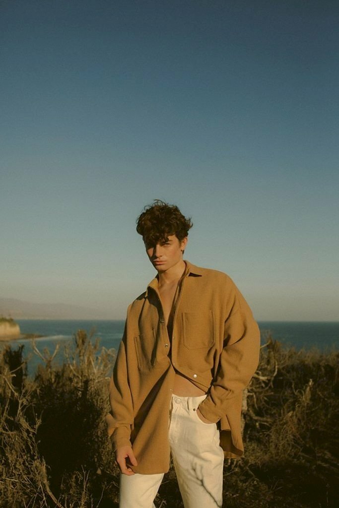 Tạo dáng đứng giữa không gian thiên nhiên với một tay đút túi quần, tóc rối trong gió