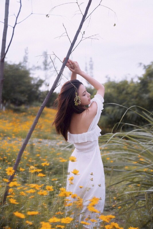 Tạo dáng đứng quay lưng, mặt hơi nghiêng qua vai hướng về ống kính, hai tay đưa lên cao vịn vào nhau