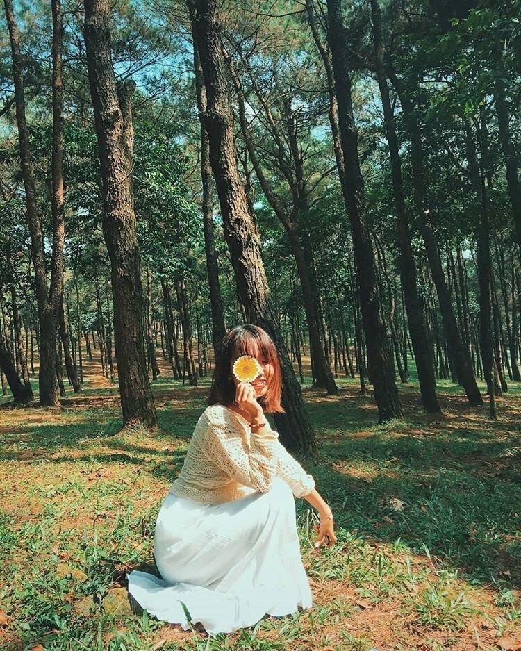 Tạo dáng ngồi nghiêng trên 02 chân, một tay duỗi tự nhiên, một tay cầm một bông hoa che một phần gương mặt