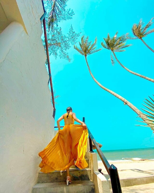 Tạo dáng bước đi lên cầu thang quay lưng về phía máy ảnh, hai tay nhẹ cầm váy, chiếc váy tung bay