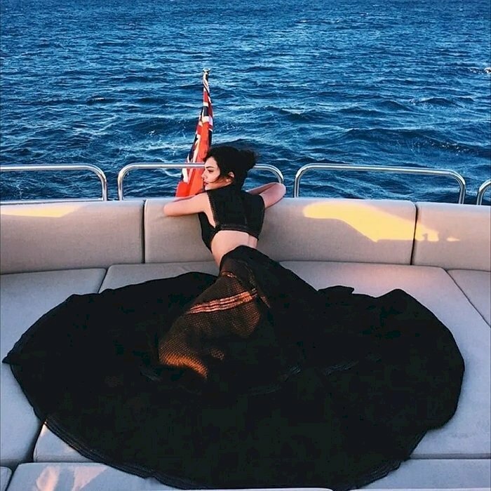 Tạo dáng với tư thế nằm quay lưng về phía ống kính, đầm trải rộng, hai cánh tay gấp lại đặt nhẹ lên thành ghế, gương mặt quay nghiêng