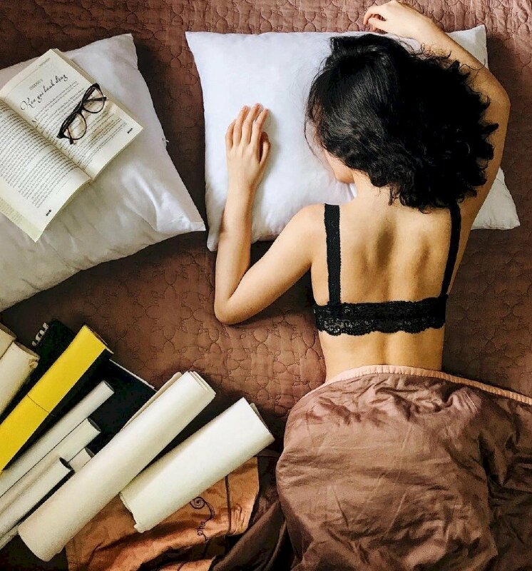 Tạo dáng nằm sấp úp nghiêng mặt xuống gối, hai tay để tự nhiên trên gối, một quyển sách đang mở được đặt cạnh bên