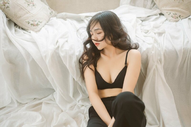 Tạo dáng ngồi tựa lưng vào chiếc giường với một chân co gối, một chân duỗi thẳng tự nhiên, hai tay đan chéo vào nhau để giữa hai chân, mặt quay nghiêng với một vài lọn tóc loà xoà che một phần gương mặt, mắt nhắm