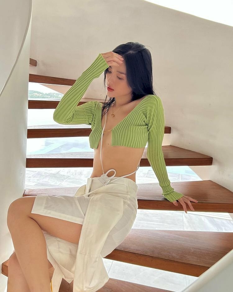 Tạo dáng chụp ảnh ngồi cầu thang với tư thế hơi nghiêng phần hông, chân duỗi nhẹ, một tay chống ngả người nhẹ về sau, một tay đưa lên nhẹ nhàng vuốt tóc, đầu nghiêng nhẹ với mắt hướng nhìn xuống, bờ môi khẽ hở