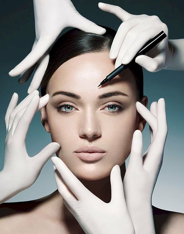 Tạo dáng như một bức tượng với gương mặt đẹp cuốn hút, mắt nhìn hướng thẳng ống kính, các bàn tay đeo găng tay trắng cầm sản phẩm quảng cáo tạo dáng như đang làm đẹp cho khuôn mặt