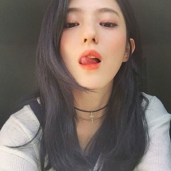 Tạo dáng với mái tóc dài xoã nhẹ, mặt hướng về máy ảnh, đưa lưỡi liếm nhẹ môi trên