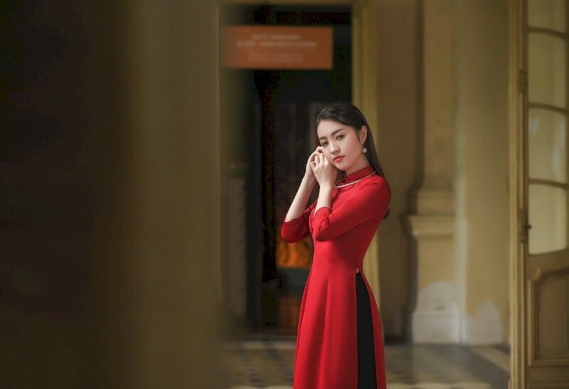 Cách tạo dáng chụp hình áo dài đứng góc nghiêng, mặt hướng về máy ảnh với ánh mắt tư lự, hai tay nhẹ đưa lên về một bên như đang đeo khuyên tai