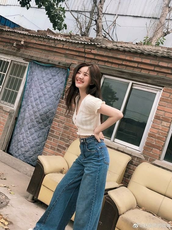 Tạo dáng hơi khom người, chân đứng hình chữ A với hai tay chống eo, góc chụp ảnh nghiêng, mặt quay hướng ống kính cười dễ thương