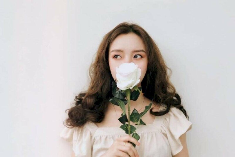 Tạo dáng tự nhiên đẹp và giản dị với nhánh hoa hồng trắng tinh khôi che mặt, mắt liếc nhìn sang phải