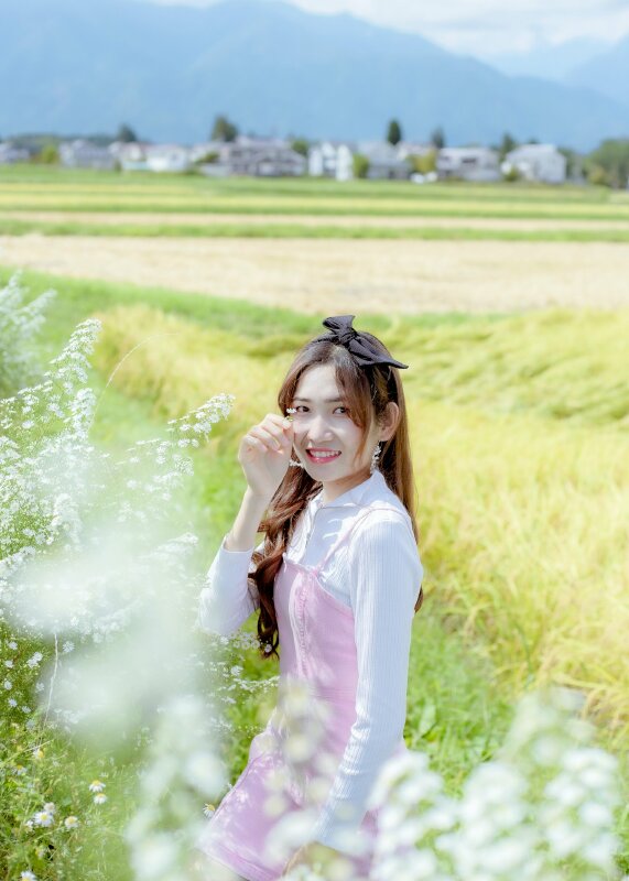 Tạo dáng xinh xắn trên cánh đồng hoa dại với góc chụp nghiêng, mặt hướng vè ống kính, miệng cười tưới mắt nhìn camera