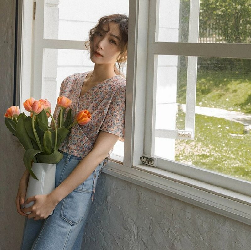 Cách tạo dáng đẹp chụp với bình hoa tulip màu cam, dáng đứa thả tự nhiên tựa lưng vào cửa sổ, đầu hơi nghiêng tựa vào song cửa sổ, mắt nhìn thẳng ống kính