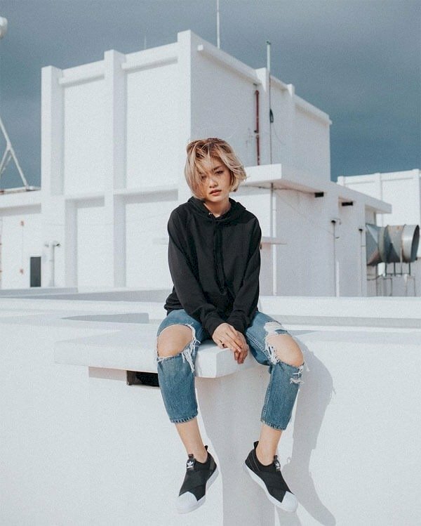 Mẫu tạo dáng ngầu chất với trang phục bụi bặm, ngồi trên một vị trí cao, hai chân buông thõng, tóc xoã bay, mắt nhìn thu hút