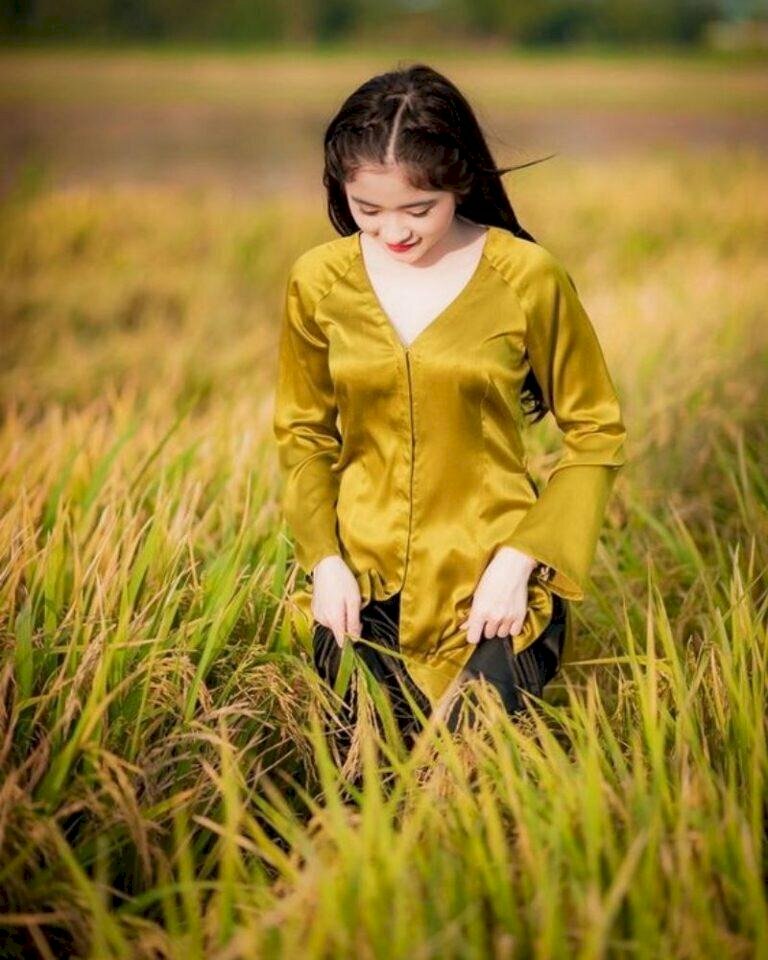 Tạo dáng đi nhẹ nhàng tự nhiên trên cánh đồng lúa, đầu hơi cúi nhẹ, hai tay khẽ nắm chiếc quần