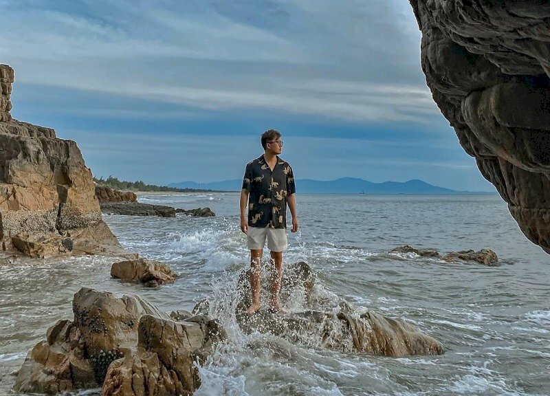 Tạo dáng đứng thật tự nhiên trên mỏm đá, hai tay buông thõng, mặt nghiêng