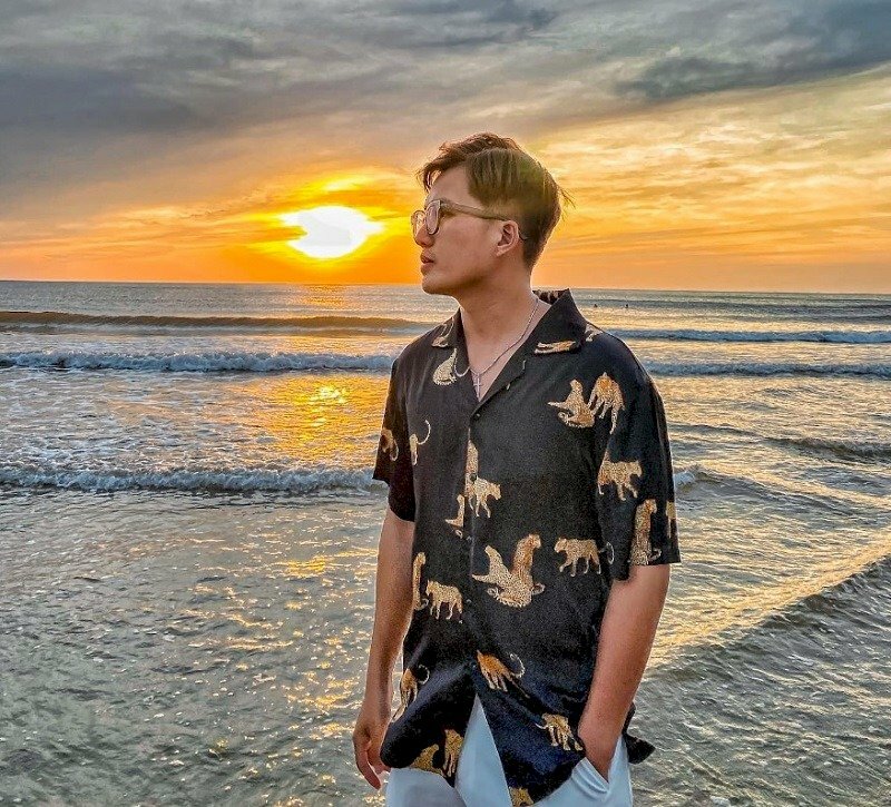 Pose ảnh với tư thế như đang bước đi, tay đút túi quần, mặt nhìn nghiêng về phía trước, bắt trọn ánh bình minh đang ló dạng