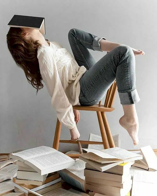 Tạo dáng độc đáo ngồi ghế ngược, người hơi ngả ra phía sau, một chân co gối để sang bên, một chân co lên gác bàn chân lên thành ghế, đầu ngả ra với quyển sách up lên che mặt