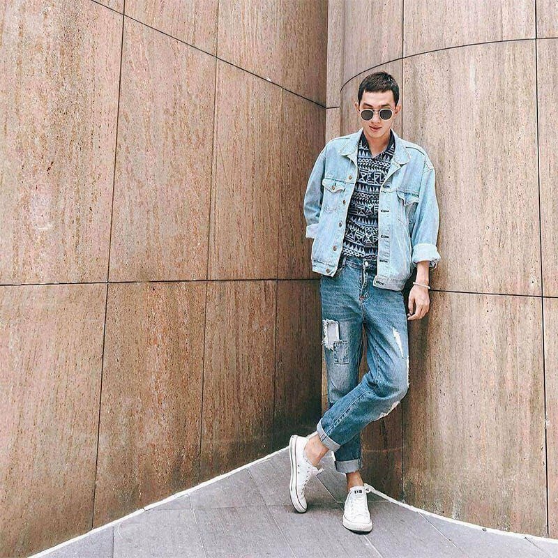 Tạo dáng chụp ảnh bắt chéo chân, đứng tựa lưng, tay đút túi quần, đeo kính đen