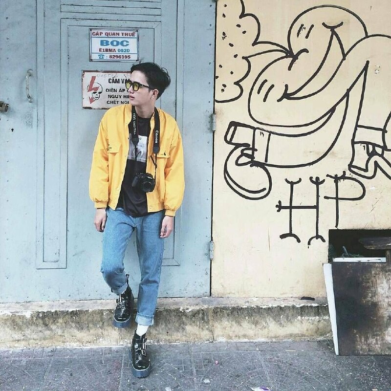 Tạo dáng dựa tường, một chân gác lên thềm, mặt nhìn nghiêng sang một phía