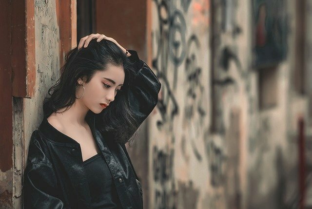 Tạo dáng tựa vào tường, một tay vuốt tóc, mặt lạnh lùng