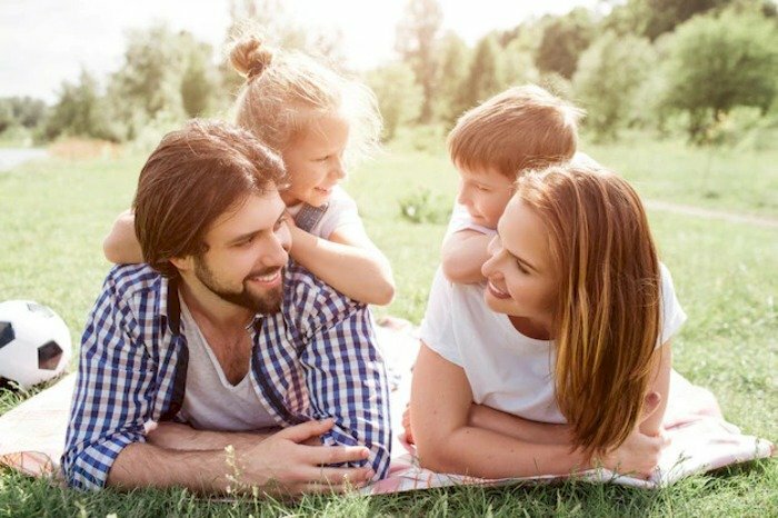 Tạo dáng chụp ảnh gia đình 4 người nằm sấp trên bãi cỏ, bé con đáng yêu nằm trên lưng ba mẹ