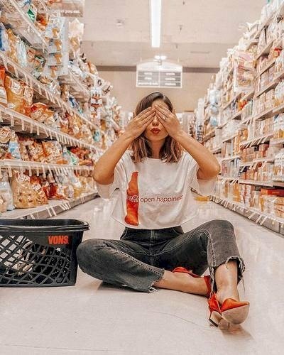 Tạo dáng ngồi bệt trên một lối đi trong siêu thị với một chân co xếp bằng, một chân duỗi tự nhiên, hai tay đưa lên che mắt, miệng chu nhẹ đáng yêu