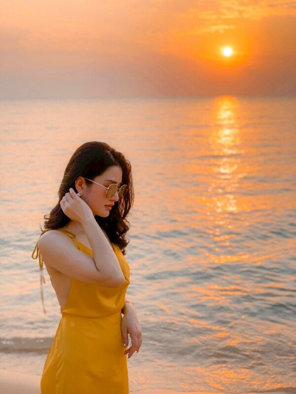 Góc chụp nghiêng, tạo dáng đứng với góc mặt hơi cúi nhẹ, một tay khẽ đưa vuốt tóc, một tay buông lơi tự nhiên