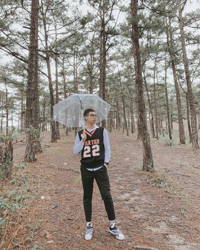 Tạo dáng đứng chân chữ A, một tay đút túi quần, một tay cầm để dù ra sau, mặt quay nghiêng nhìn về một phía