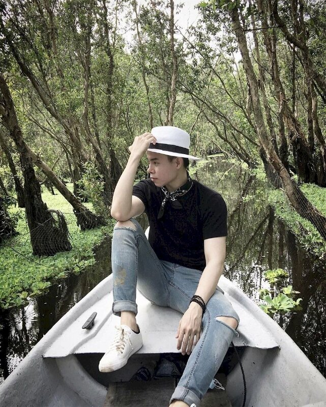 Tạo dáng với tư thế ngồi ở đầu mũi xuồng, một chân co, tay chống gối để nhẹ lên mũ, một chân duỗi tự nhiên, mặt quay nghiêng