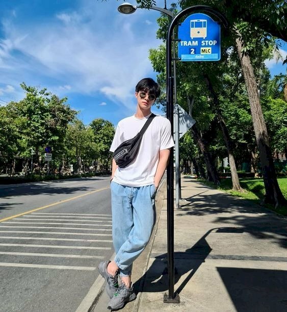 Tạo dáng hai tay xỏ túi quần, chân bắt chéo, dựa tạm vào một chiếc cột bên đường