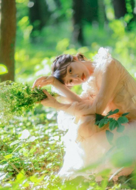 Tạo dáng ngồi với đầu cúi nhẹ trên hai tay co đặt trên gối, tay cầm bó hoa dại