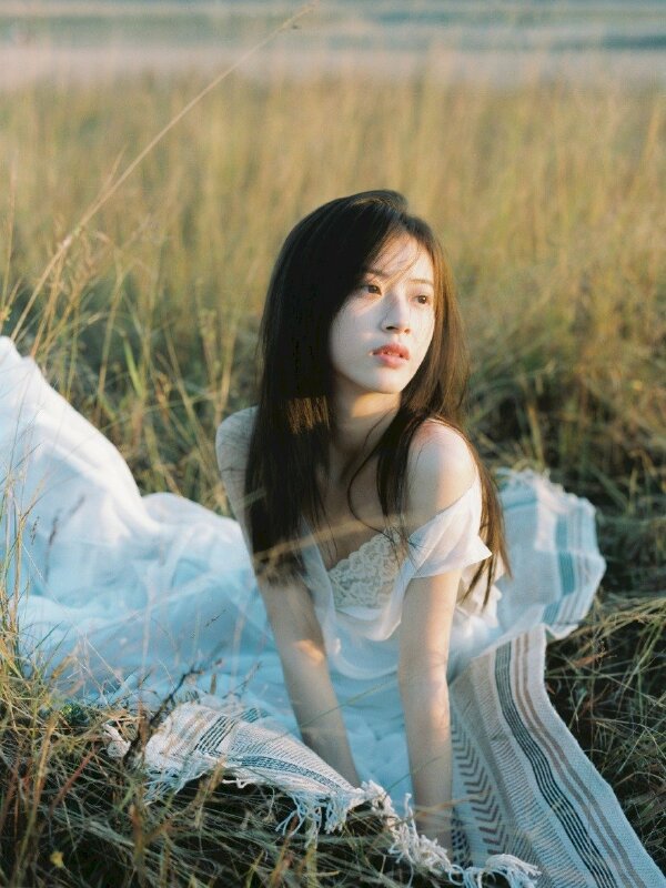 Tạo dáng ngồi trên thảm cỏ với tư thế hơi chúi người về phía trước, hai tay chống duỗi nhẹ, tóc xoã bay trong gió