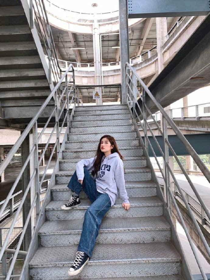 Tạo dáng người ngồi lệch một bên trên cầu thang, một chân co gối, một chân duỗi thẳng, một tay ôm chân co, một tay chống lên bậc thang