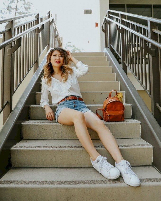 Cách tạo dáng ngồi với hai chân duỗi nhẹ, người hơi ngả ra sau, một tay đặt trỏ lên bậc thang, một tay nhẹ đưa lên tóc