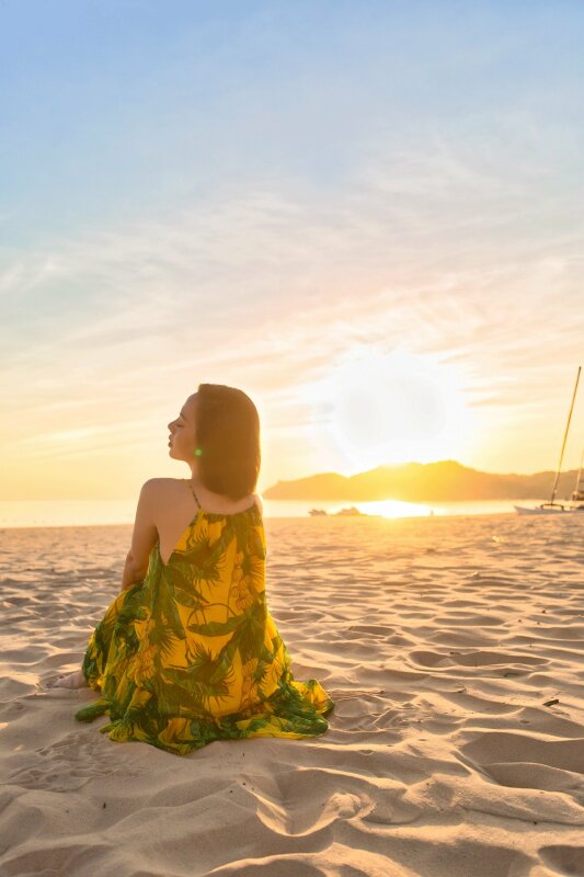 Tạo dáng ngồi trên cát, thả lỏng cơ thể thật tự nhiên, mặt quay nghiêng