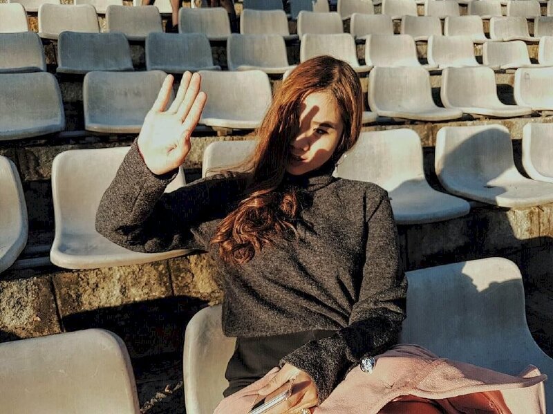 Tạo dáng ngồi bắt chéo chân lấy tay giơ lên che nhè nhẹ, một tay để hờ hững trên đùi, đầu hơi nghiêng với mắt nhìn xa xăm về phía trước