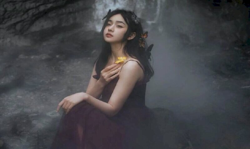 Tạo dáng cô gái ngồi góc nghiêng mặt hơi hướng cằm lên mắt nhìn xa xăm, một tay đặt nhẹ lên gối, một tay đưa lên vịnh nhẹ bờ vai, tóc dài buông xoã