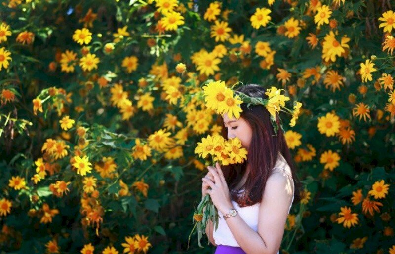 Tạo dáng chụp góc nghiêng với vòng hoa đội đầu và tay nâng nhẹ bó hoa dã quỳ che mặt e ấp