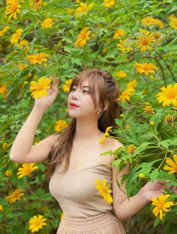 Tạo dáng đứng nhẹ nhàng với một tay đưa lên chạm vào hoa, một tay đưa ngang, mắt nhìn hoa