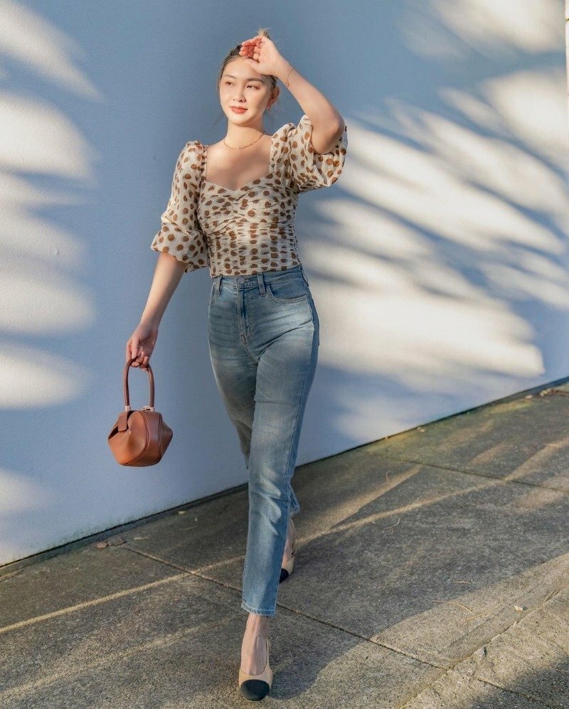 Tạo dáng sải bước đi dạo với một tay nhẹ đưa lên như che nắng, một tay cầm chiếc túi nhỏ thời trang đánh tay tự nhiên